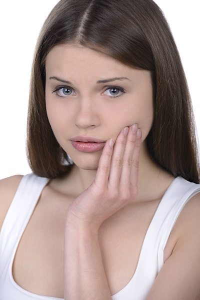 Woman with straight dark brown hair touches face in discomfort.